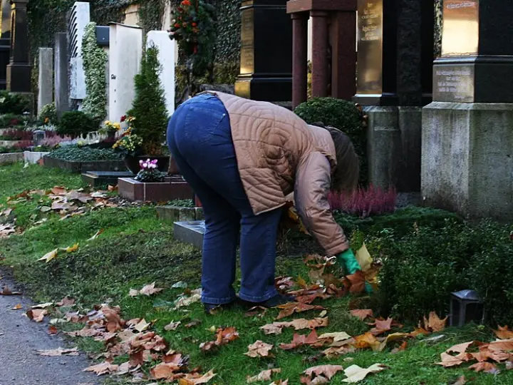 Osoba zbierająca jesienne liście przy grobie